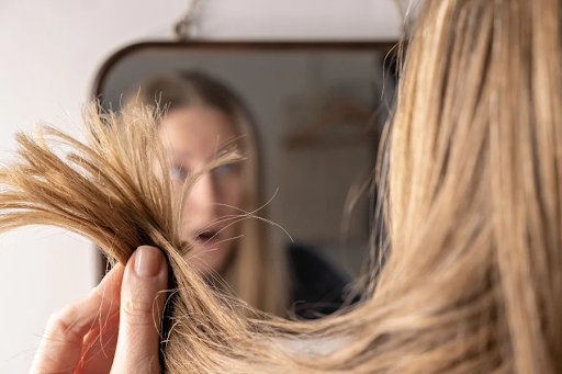 Woman noticing split ends in mirror—common signs of hair damage and how to get rid of split ends at home.