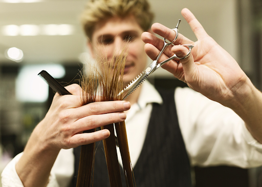 Hair stylist trimming inches of dead ends hair—traditional method to remove damage and split ends.